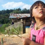 a young girl in a pink outfit looks at the camera while holding a plant