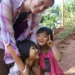 a woman hugs two small children on a dirt road