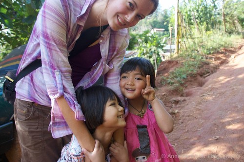 a woman hugs two small children on a dirt road