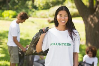 A volunteer holds a trash bag and smiles outside
