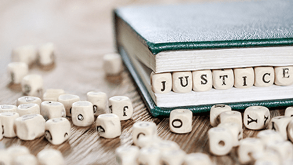Small blocks of letters form the word "Justice" wedged inside the pages of a book.