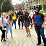 A group of students smile for a picture near campus buildings