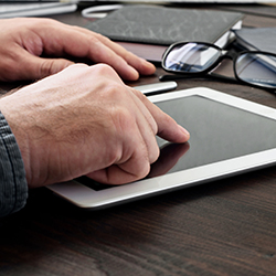 Someone touches the screen of a dark iPad on their desk