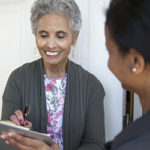 A mature woman signs a piece of paper for another woman off frame