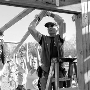 A group of volunteers lift their arms in unison to lift a board in a black and white image