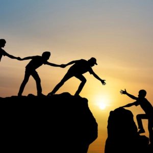 Three people working together to help someone get across a chasm at sunset