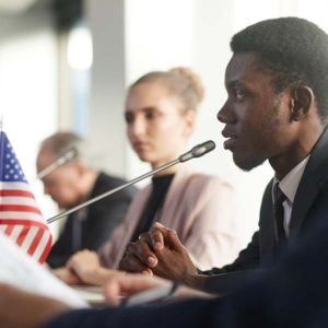 a man leans into a microphone adorned with a small American flag to speak