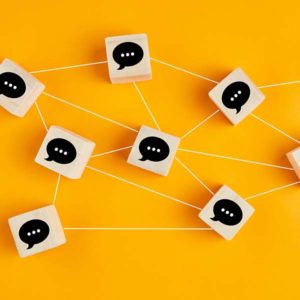elipses in quote bubbles printed on wooden blocks and interconnected by white string on a vibrant yellow table
