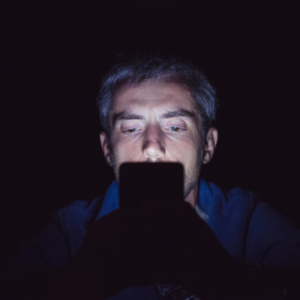 A man's face is illuminated by the glow of his phone in a dark room